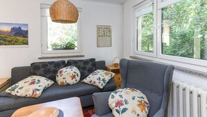 A cozy living room with a sofa, a table, and a window with a view of greenery. - Holiday Home 'Krohse' with Shared Garden and Wi-Fi (Potsdam)