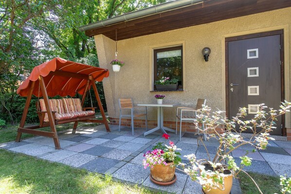A patio with a swing chair, a table, chairs, and potted plants.