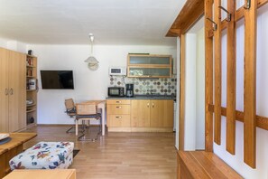 Cocina compacta con armarios de madera, microondas, cafetera y televisor montado en la pared.