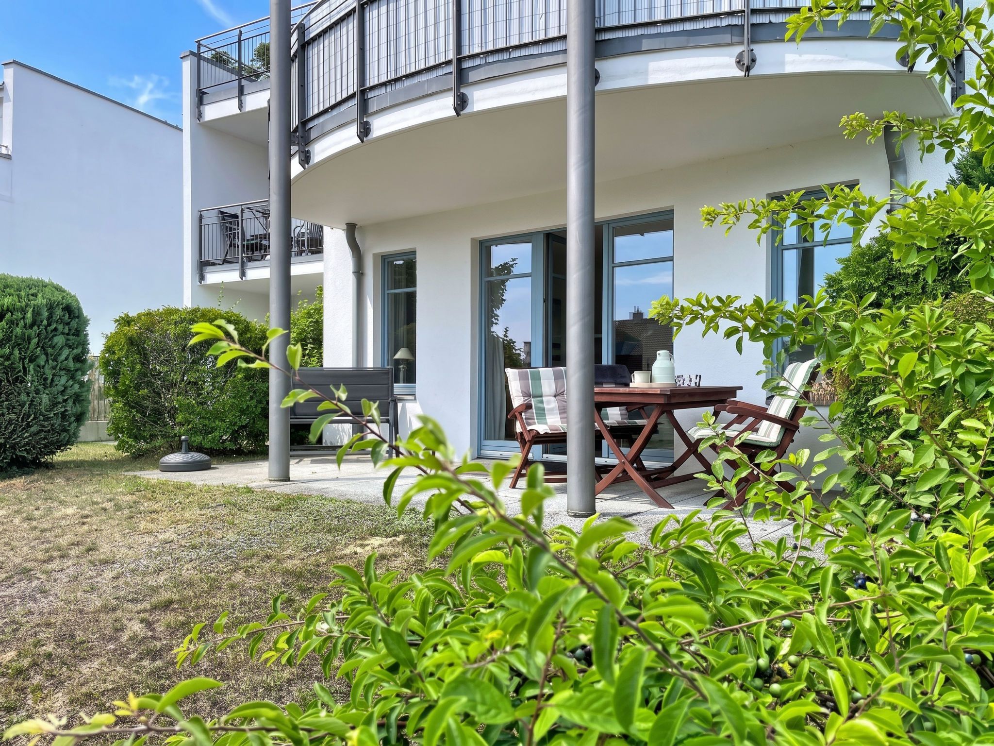 Ein modernes, zweistöckiges Gebäude mit Balkon, Sitzgelegenheit im Freien und einem gepflegten Garten.