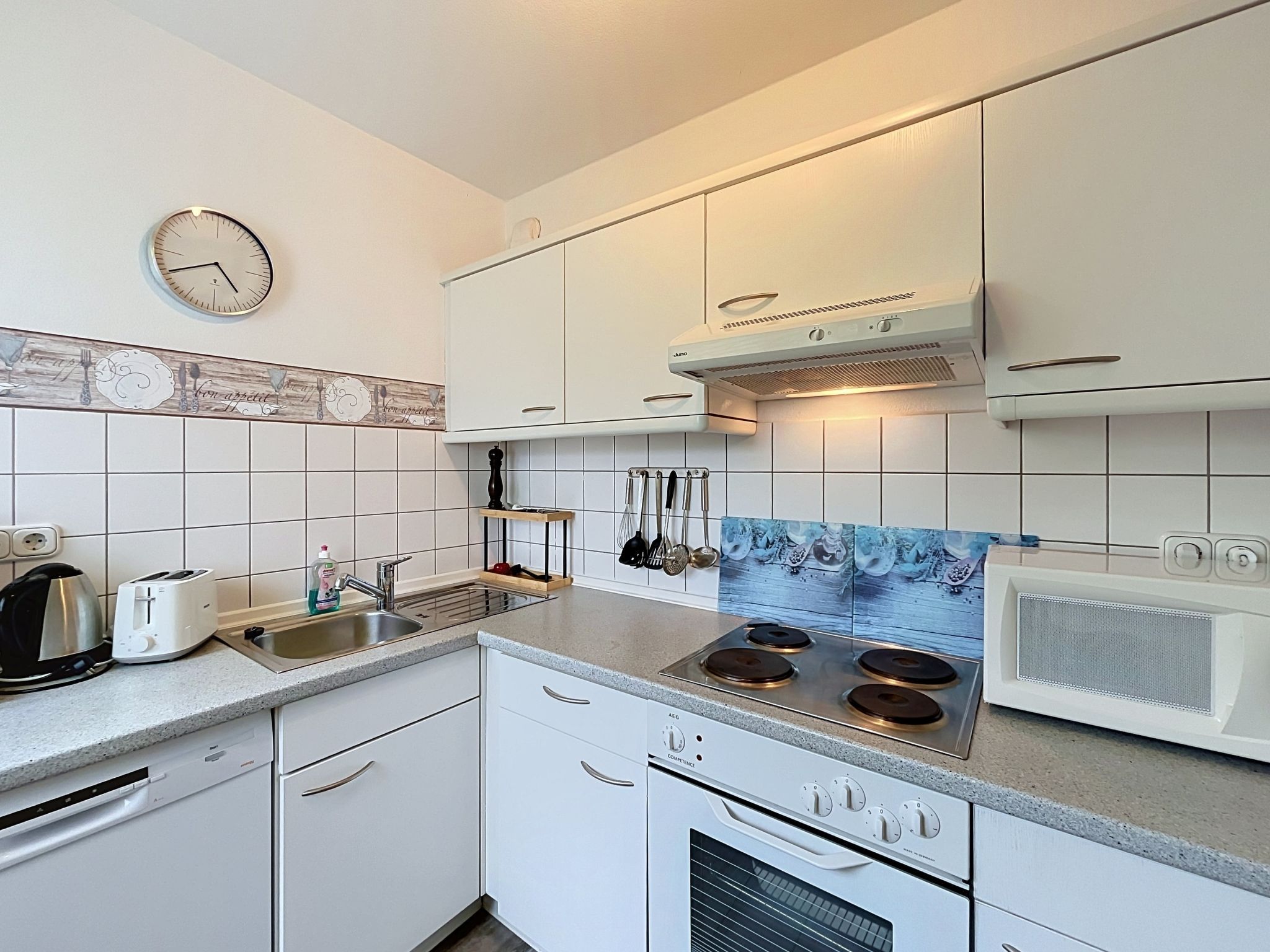 A modern kitchen with white cabinets, a stainless steel sink, a built-in stove, and a clock on the wall.