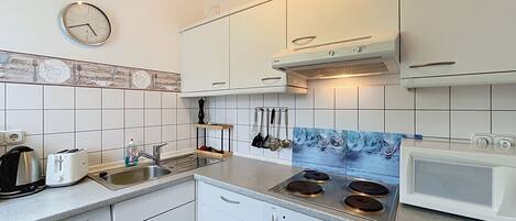 A modern kitchen with white cabinets, a stainless steel sink, a built-in stove, and a clock on the wall.