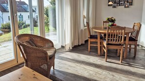 A dining area with a wooden table and chairs, large windows with curtains, and a view of houses outside.