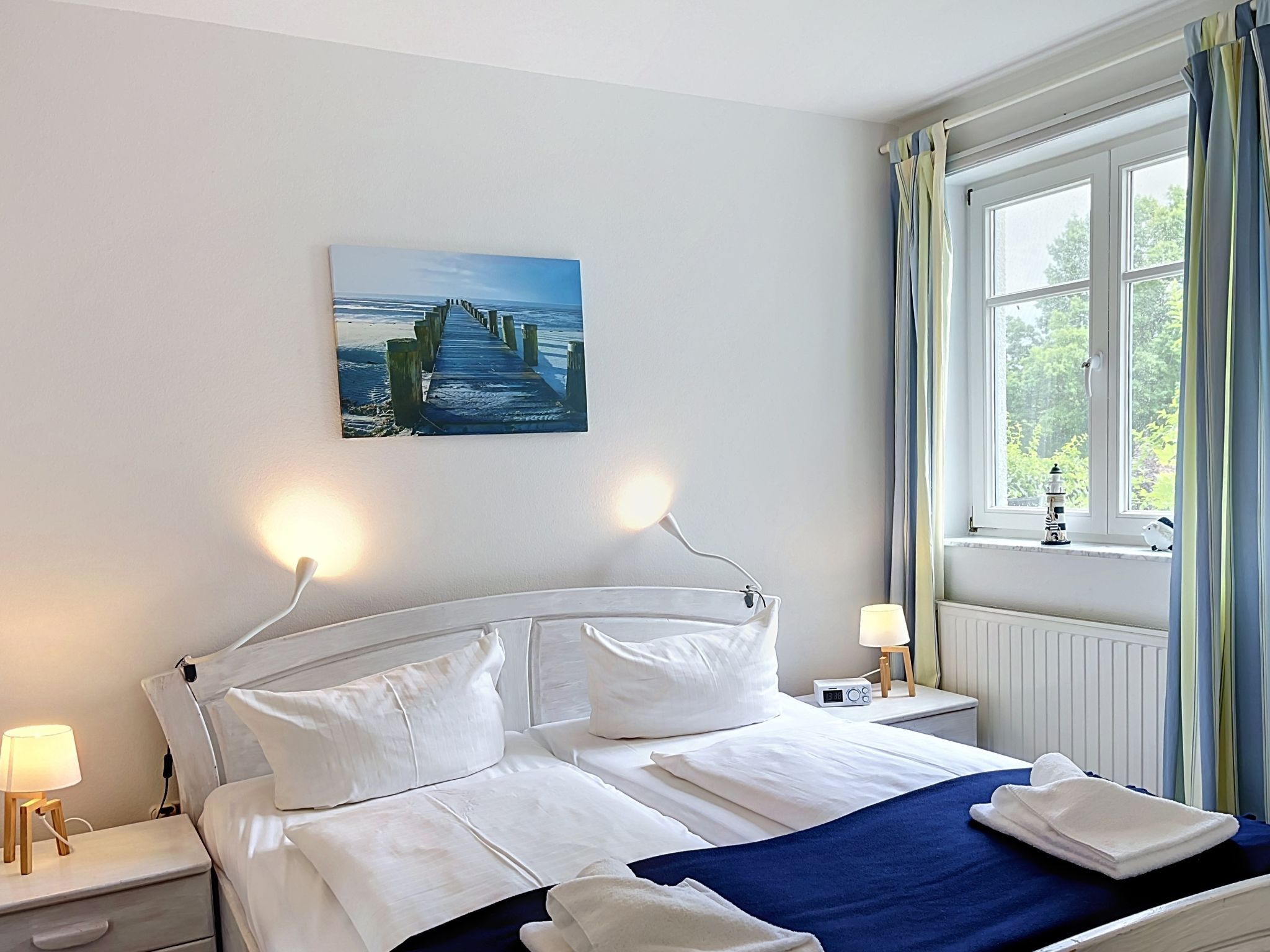 Une chambre d’hôtel avec un lit, des lampes de chevet, un tableau au mur et une fenêtre avec des rideaux.
