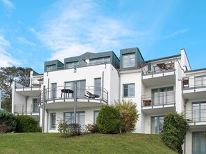 Ein modernes Mehrfamilienhaus mit Balkonen, einer flachen Dachterrasse und einem gepflegten Rasen.