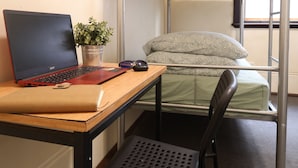 Ein Stockbett mit einem Laptop und einem Stuhl in einem Zimmer mit Fenster und Klimaanlage.