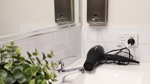 Ein Badezimmer mit einem weißen Waschbecken, einem Topfpflanzen, einem Haartrockner und zwei an der Wand befestigten Seifenspendern.