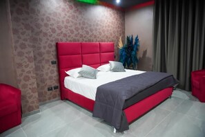 Un dormitorio moderno con cama roja, ropa de cama blanca y una manta gris.