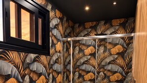 A modern bathroom with a leaf-patterned wallpaper, a wooden floor, a white sink, and a glass shower enclosure. - HOTEL EL PAMAS (Mugnano di Napoli)