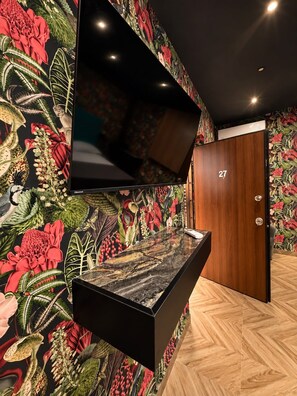 Interior moderno com televisão de tela plana na parede, porta de madeira com o número 27 e piso com padrão losango.