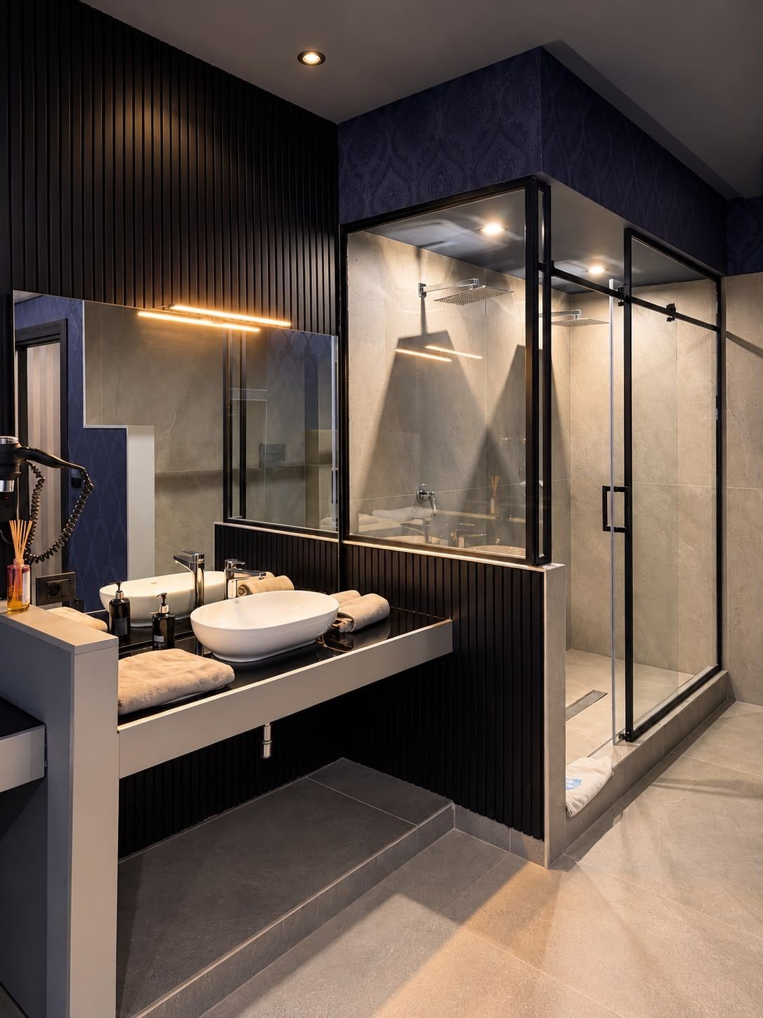 Ein modernes Badezimmer mit einer Glaskabine zur Dusche, einem Waschtisch mit großem Spiegel und einem integriertem Waschbecken.