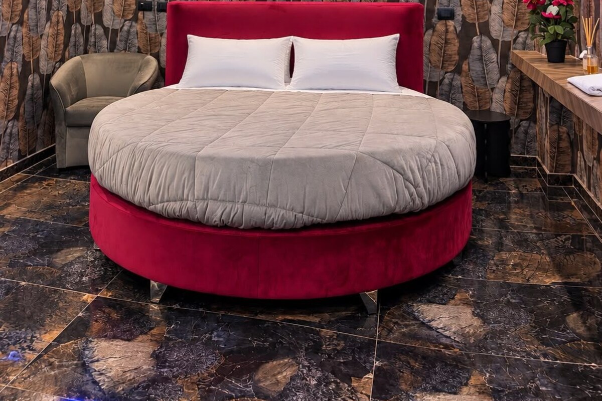 A modern bedroom with a round bed, red headboard, and a patterned wallpaper.
