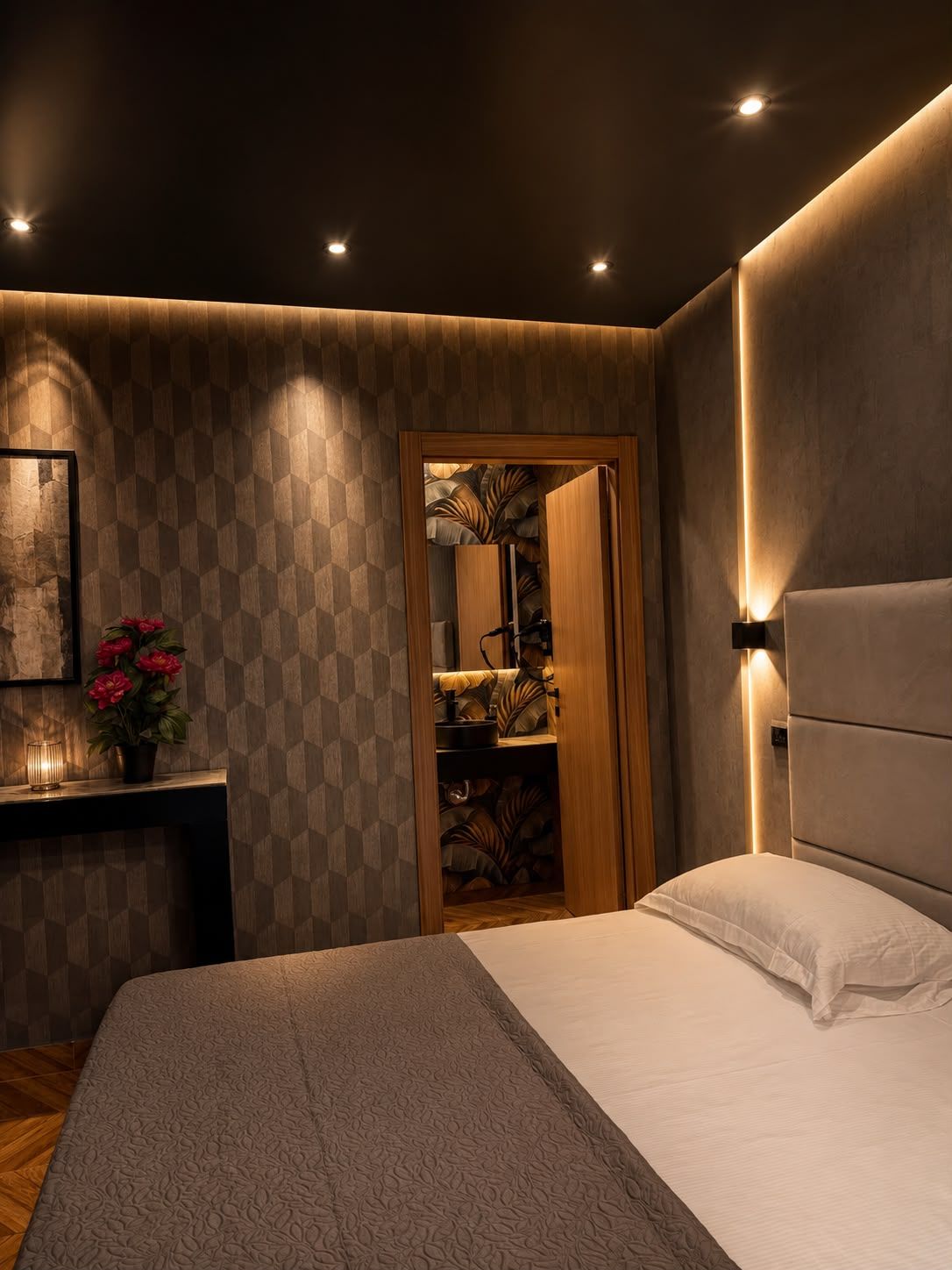 Une chambre à coucher moderne avec un grand lit, une table de chevet, une lampe fixée au mur et un miroir décoratif.