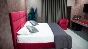 A hotel room with a red headboard, a bed with white and gray bedding, a red chair, a desk with speakers, and a large window with curtains. - HOTEL EL PAMAS (Mugnano di Napoli)