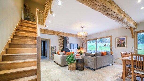 Un vaste espace de vie comprenant un escalier en bois, une cheminée, un ensemble de canapés et une table à manger.