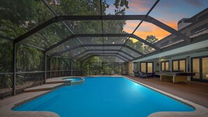 Une piscine intérieure couverte, dotée d’un toit en verre, entourée d’un patio aménagé avec des sièges et une table de billard.