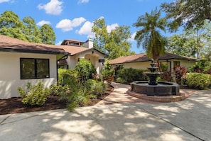A residential property with a paved driveway, a fountain, and lush landscaping. - Tampa Oasis | Private Pool + Sauna | Sleeps 14 (Temple Terrace)