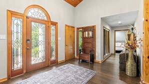 Un couloir avec des portes en bois, un banc, un tapis et un vase contenant des fleurs séchées.