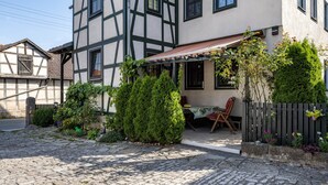 Ett traditionellt hus med korsvirkesfasad, en täckt uteplats, stenläggning och ett trästaket.