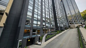 Un moderno edificio de rascacielos con varios pisos, grandes ventanales y una entrada visible con una escalera que baja al nivel de la calle.