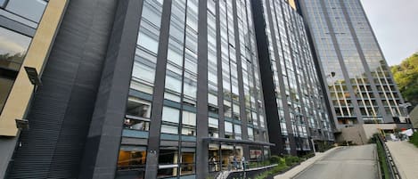 A modern high-rise building with multiple floors, large windows, and a visible entrance with a staircase leading to the ground level.