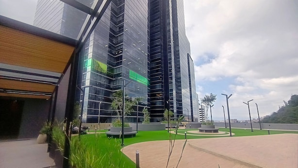A modern building with reflective glass facade, a landscaped area with greenery, and a paved walkway. - Loft 820 (Bogotá)
