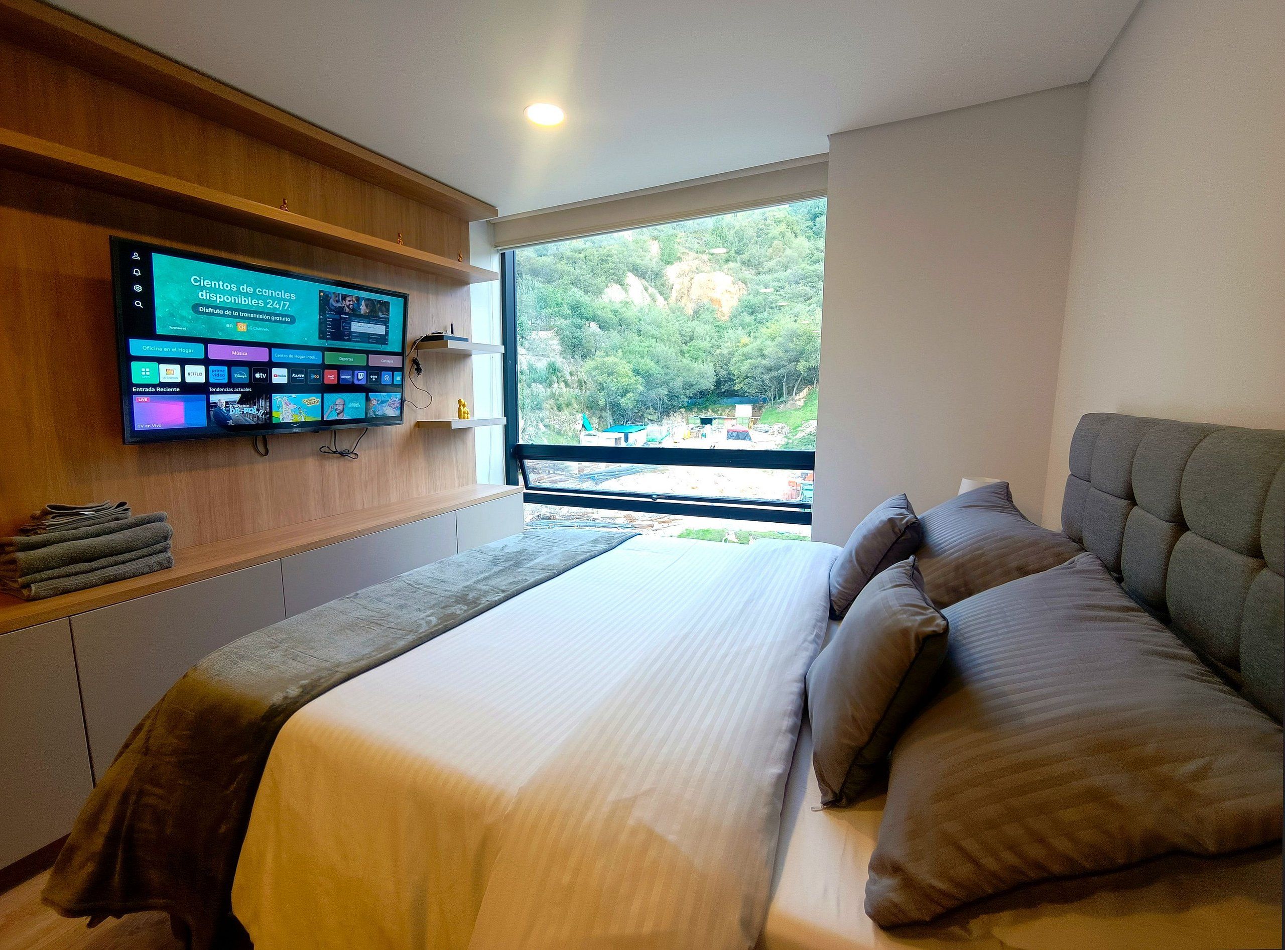 Une chambre d’hôtel moderne dotée d’un grand lit, d’un téléviseur à écran plat fixé au mur et offrant une vue sur l’extérieur grâce à une grande fenêtre.