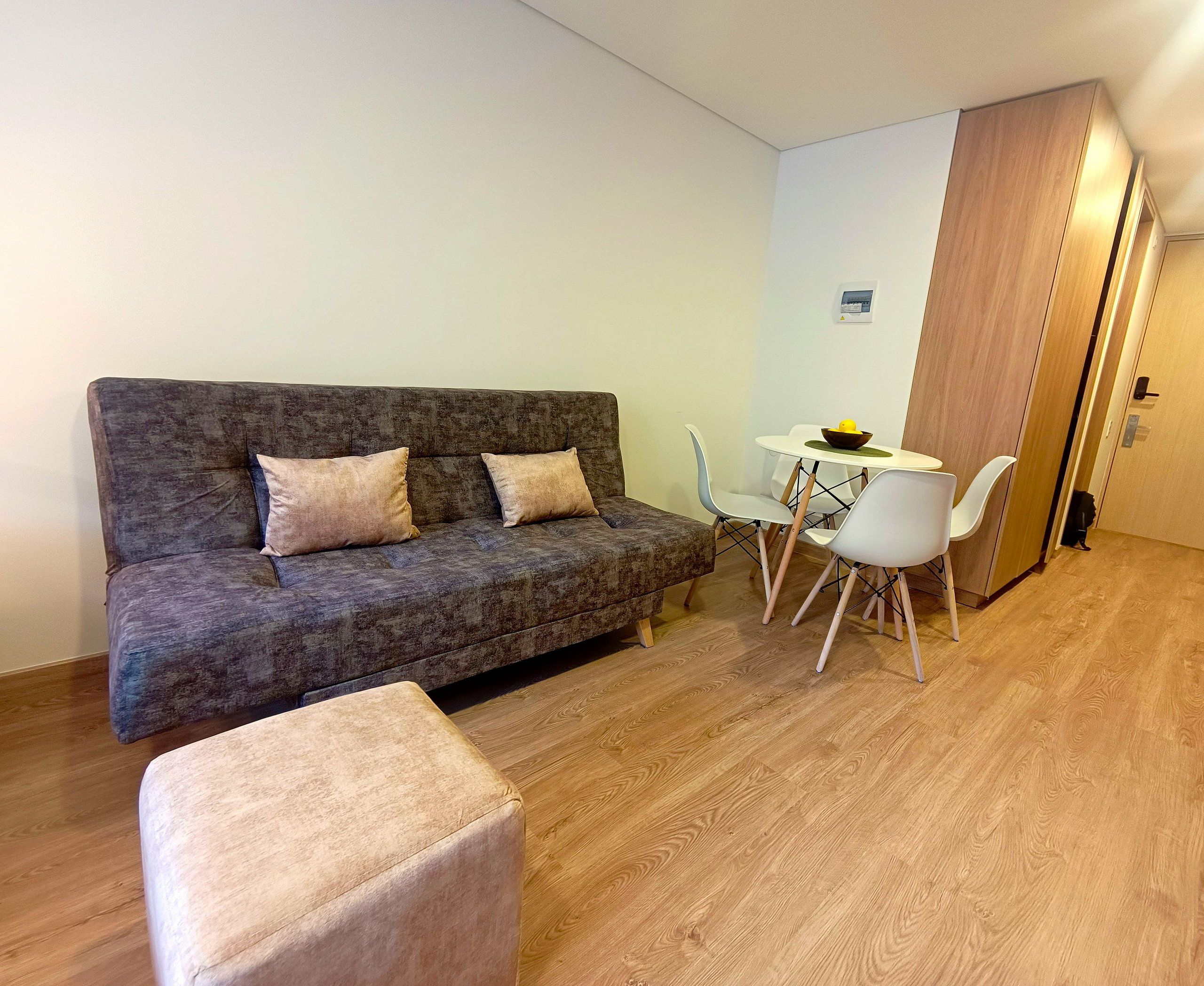 Un espacio habitable compacto con un sofá gris, una mesita redonda con un bol y una silla blanca.