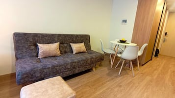 Un espacio habitable compacto con un sofá gris, una mesita redonda con un bol y una silla blanca.