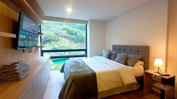 Un dormitorio moderno con una cama grande, un televisor en la pared y vistas a zonas verdes.