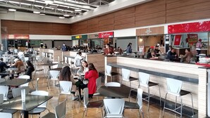 Un amplio comedor interior con varias mesas y sillas, una barra con un miembro del personal y diferentes puestos de comida al fondo.