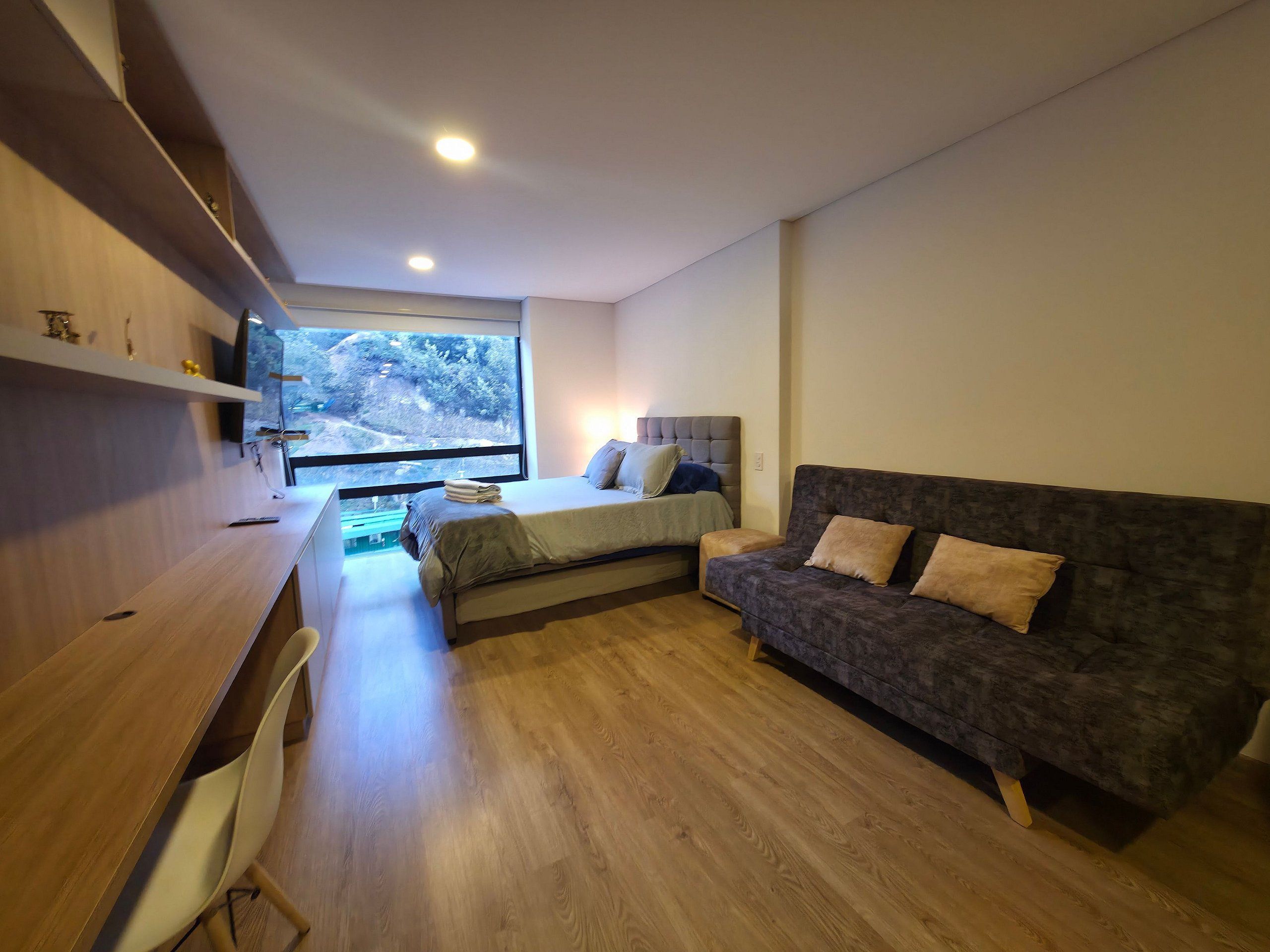 Un dormitorio moderno con cama, sofá, escritorio y un ventanal amplio.