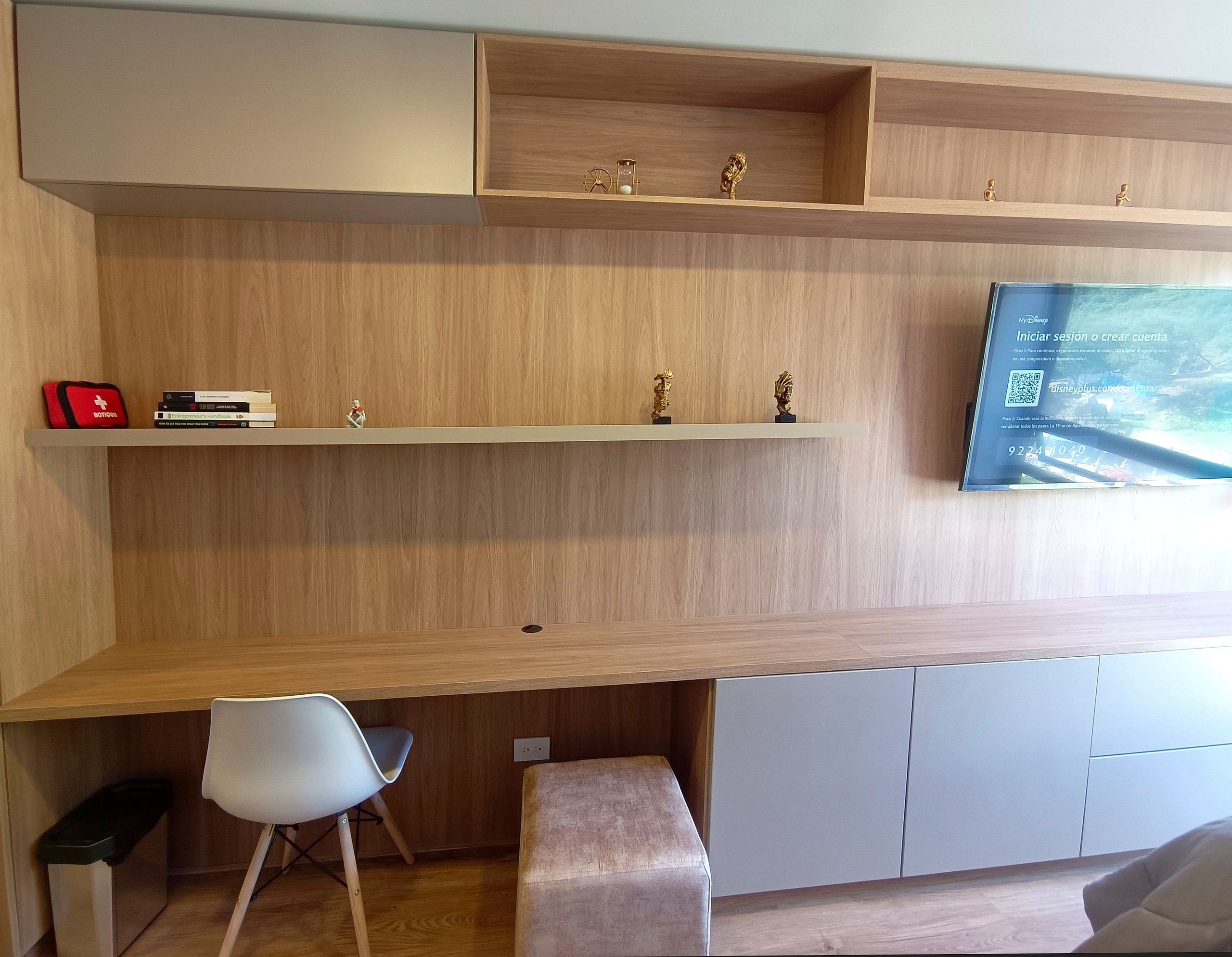 Ein modernes Zimmer mit einem Holztisch, einem weißen Stuhl und einer Bank. Über dem Tisch befinden sich Regale mit Büchern und Dekoration.