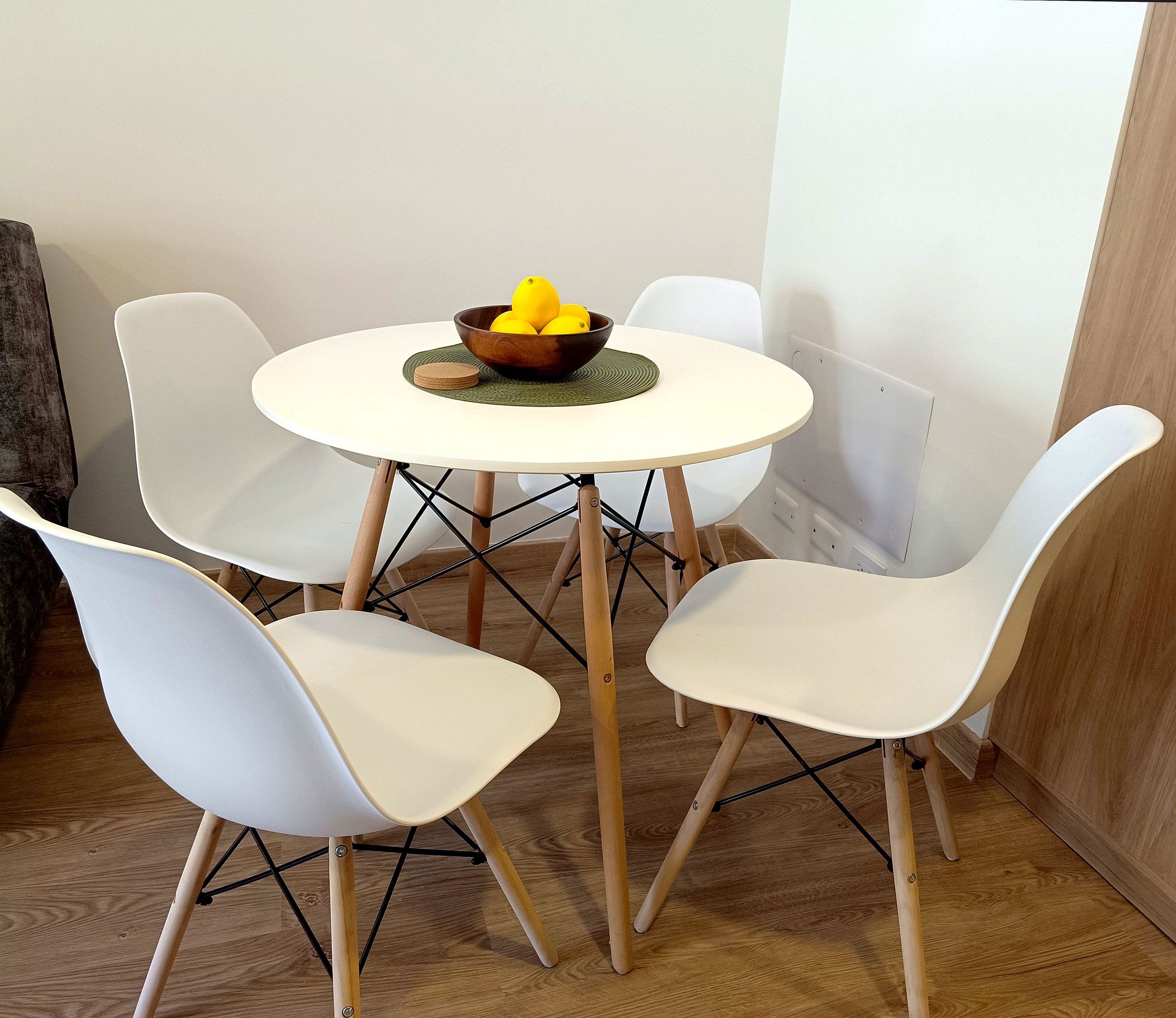 Un pequeño comedor con una mesa redonda, cuatro sillas blancas y un bol de limones sobre la mesa.