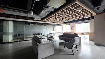 A modern office space with a glass-walled meeting room, grey sofas, and a large window providing natural light.