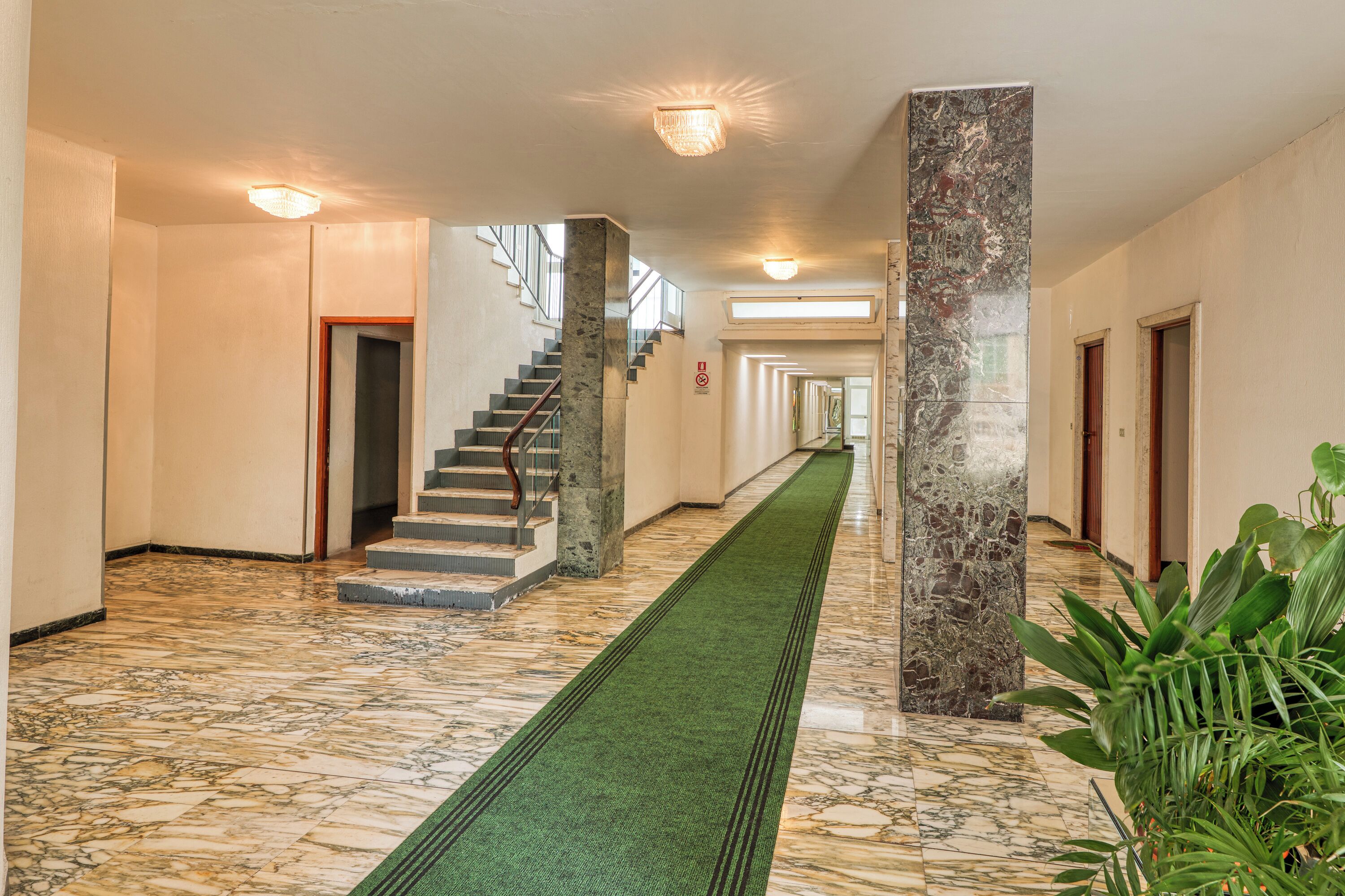 Eine Hotelhalle mit Marmorboden, einem pflegeleichtem Teppichweg, einer Treppe und einer großen Säule.