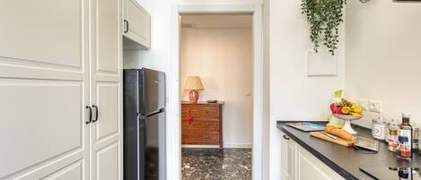 A kitchen with white cabinets, a black refrigerator, a wooden dresser, and a countertop with various items.