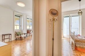 Amplia habitación con piso de madera, cama con colcha estampada, lámpara de pie y una silla con cojín verde.
