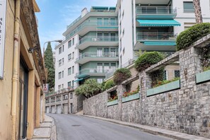 Una calle estrecha bordeada por edificios de varios pisos con balcones, muros de piedra y plantas en macetas.