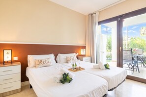 Una habitació d'hotel amb dos llits, una tauleta de nit amb una làmpada, una taula petita amb una bandeja de menjar i vistes a un jardí a través d'una porta corredissa.