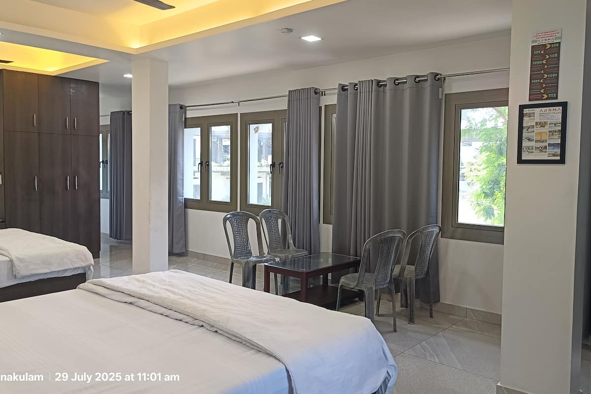 A hotel room with two beds, a dining table with chairs, and large windows with curtains.