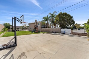 Cortile residenziale con canestro da basket, scivolo e area giochi coperta.
