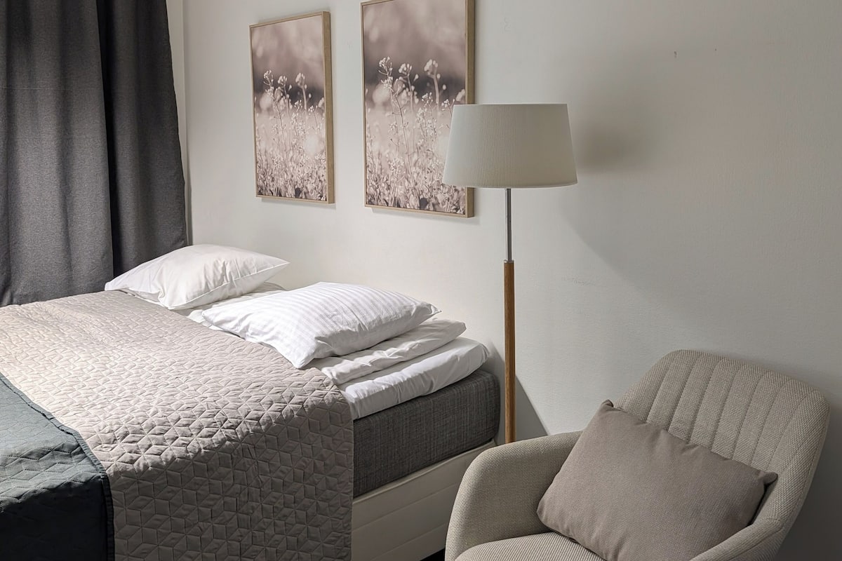 A modern bedroom with a bed, a chair, and two wall-mounted pictures.