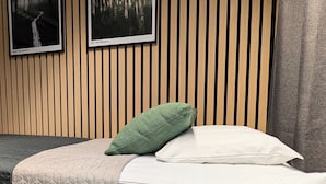 Un llit ben fet amb un sobre mullat, una almoçada verda i una almoçada blanca. Hi ha una planta en test al primer pla. La habitació té panells de fusta a la paret i dos quadres emmarcados sobre el llit.