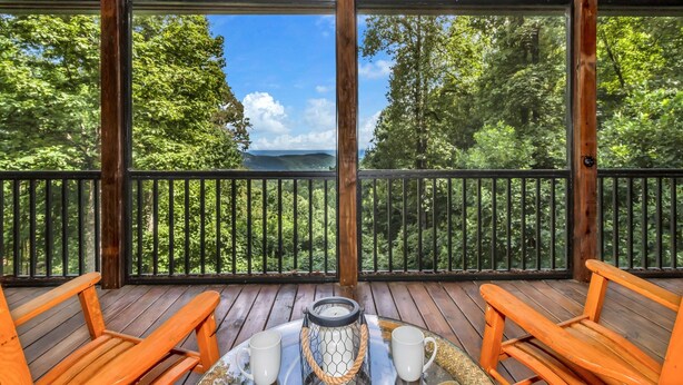 A wooden deck with two orange chairs and a table with a lantern and two white mugs. - Gateway Getaway with Mountain Views and Fireplace (Old Fort)