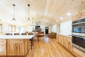 A spacious kitchen with wooden cabinets, a large island, and a built-in oven. - Shady Rest Cabin #12, Brand-New 4-Bedroom Lakeside Cottage (Rhinelander)