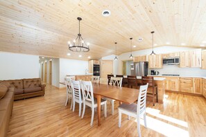 A spacious kitchen with wooden cabinets, a dining table, and chairs. - Shady Rest Cabin #12, Brand-New 4-Bedroom Lakeside Cottage (Rhinelander)