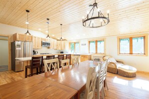 A spacious kitchen with wooden cabinets, a stainless steel refrigerator, a microwave, and a dining area with a wooden table and chairs. - Shady Rest Cabin #12, Brand-New 4-Bedroom Lakeside Cottage (Rhinelander)