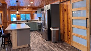 Een moderne keuken met houten balken in het plafond, een centraal eiland, roestvrijstalen apparatuur en een schuifdeur van glas.