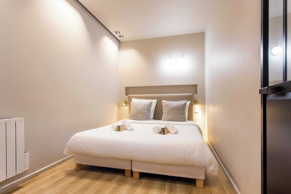 A neatly made bed with pillows and towels, a bedside table, and a wall-mounted light fixture.